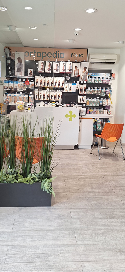 Dos farmac&eacute;uticos sonr&iacute;en mirando al frente con estanter&iacute;a de productos detr&aacute;s